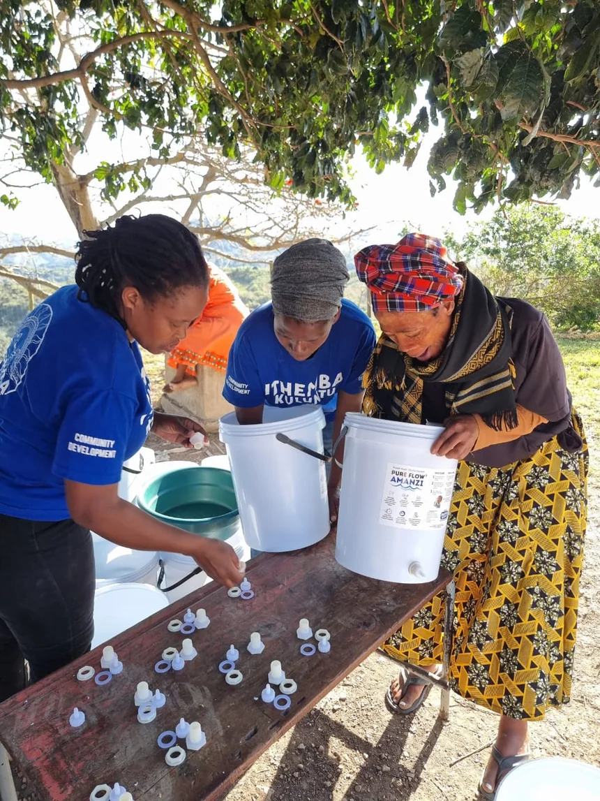 PureFlow fieldworkers demonstrating water-filter parts and assembly with women at an outdoor training table