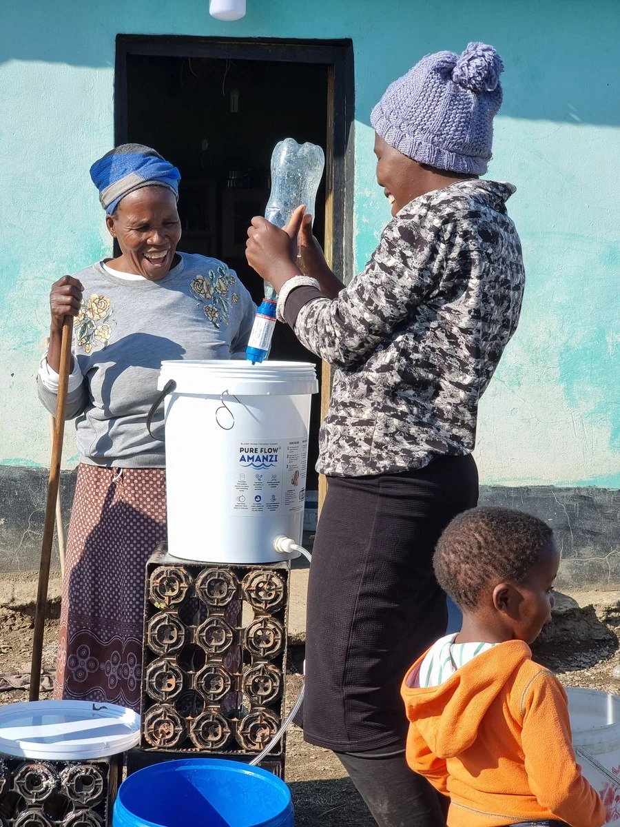 A resident, a local facilitator and a young child beside a PureFlow water-filtration system at a rural home