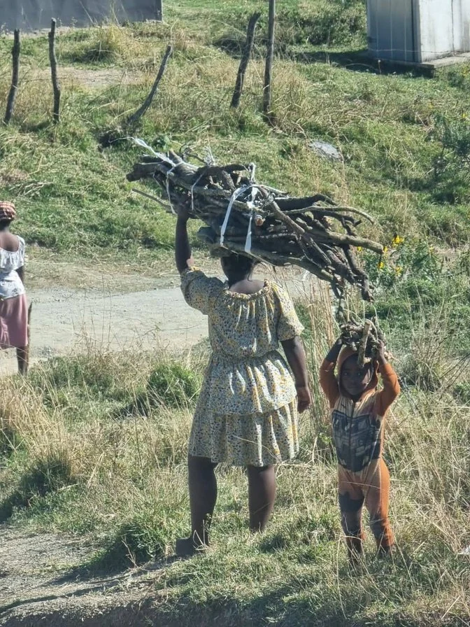 A woman and child carrying collected firewood through a rural community
